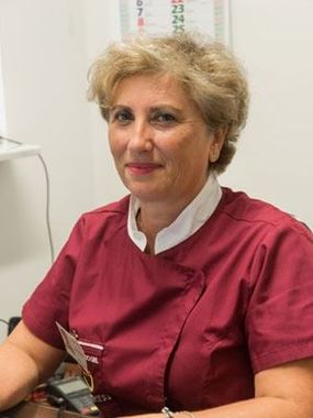 Operatore sanitario in camice bordeaux seduto a una scrivania, rivolto verso la telecamera.