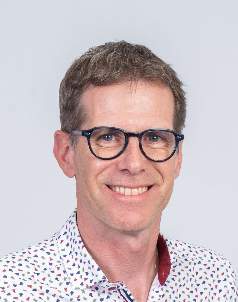 Personne aux cheveux châtain clair et portant des lunettes sourit chaleureusement, vêtue d'une chemise.