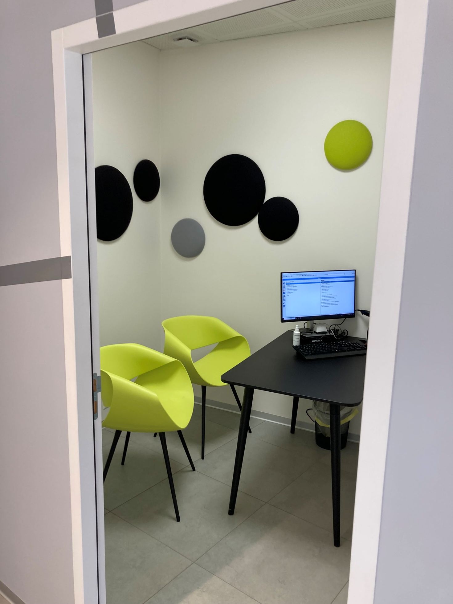 A small office with a desk, computer, and two lime green chairs, featuring circular wall accents in black, gray, and green.