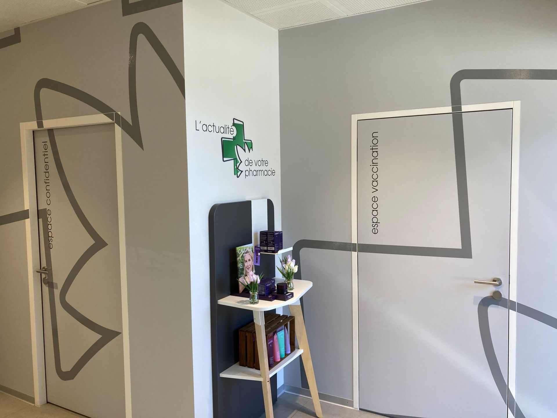 A lobby with two doors, gray walls with dark geometric line murals, and a shelf displaying various products.