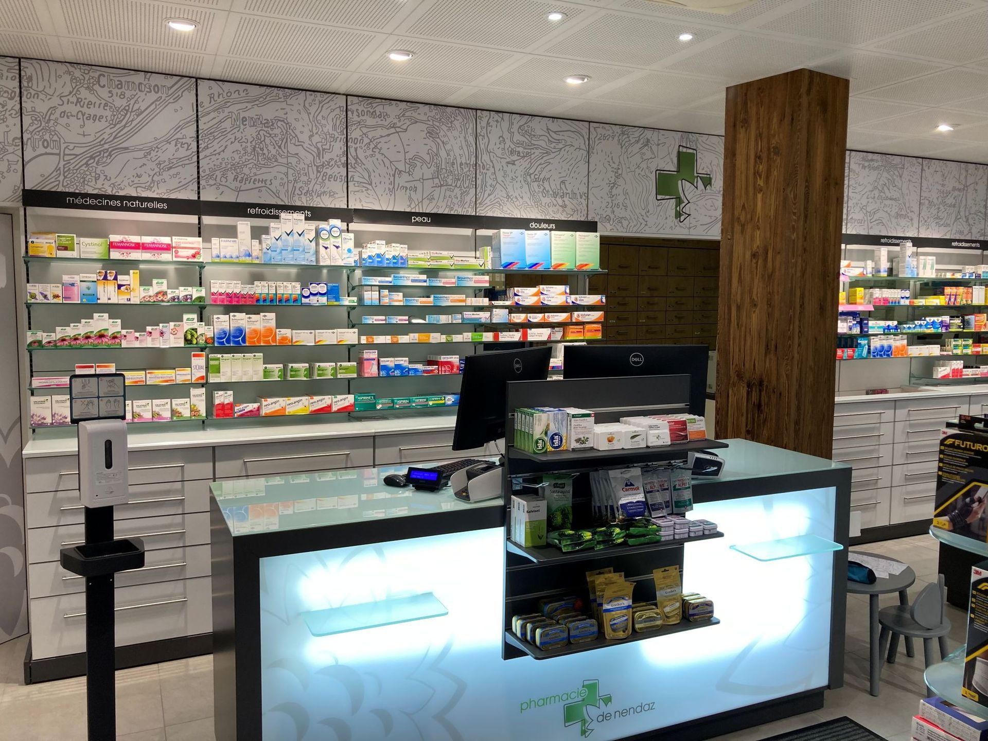 A brightly lit pharmacy counter featuring shelves stocked with medication boxes and a hand sanitizer station.