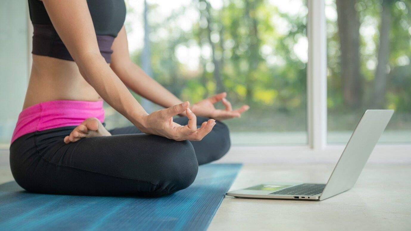 una mujer está sentada en una estera de yoga frente a una computadora portátil