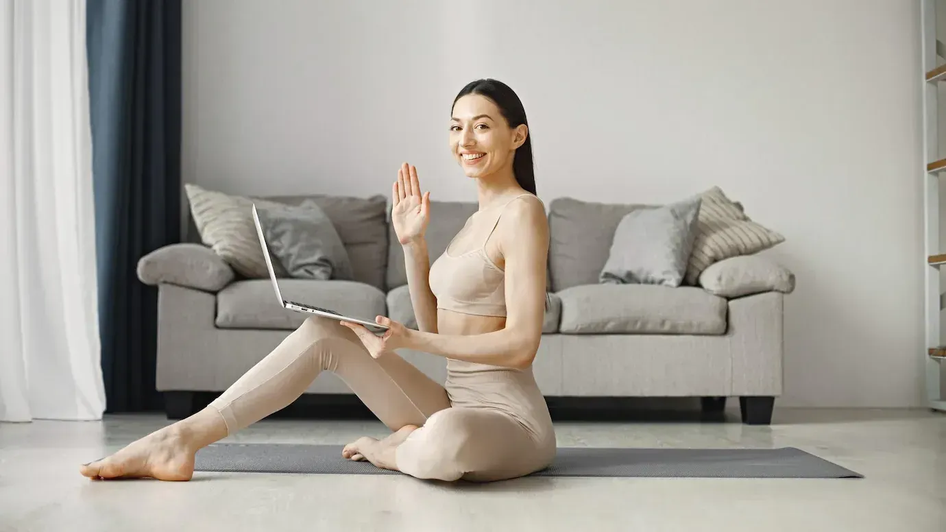 una mujer se sienta en una estera de yoga y sostiene una computadora portátil