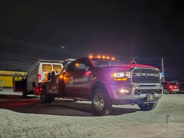 A tow truck with flashing lights towing a white van at night.