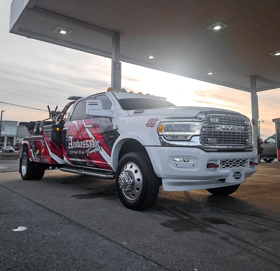 White and red tow truck parked under gas station canopy at dusk.