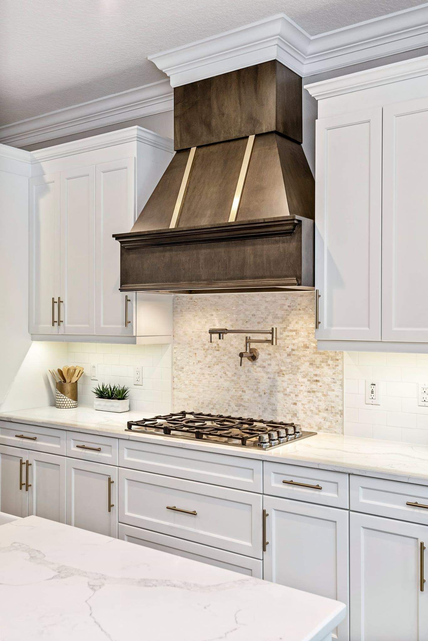 Elegant white kitchen with marble countertops, gas range, and large stainless-steel vent hood