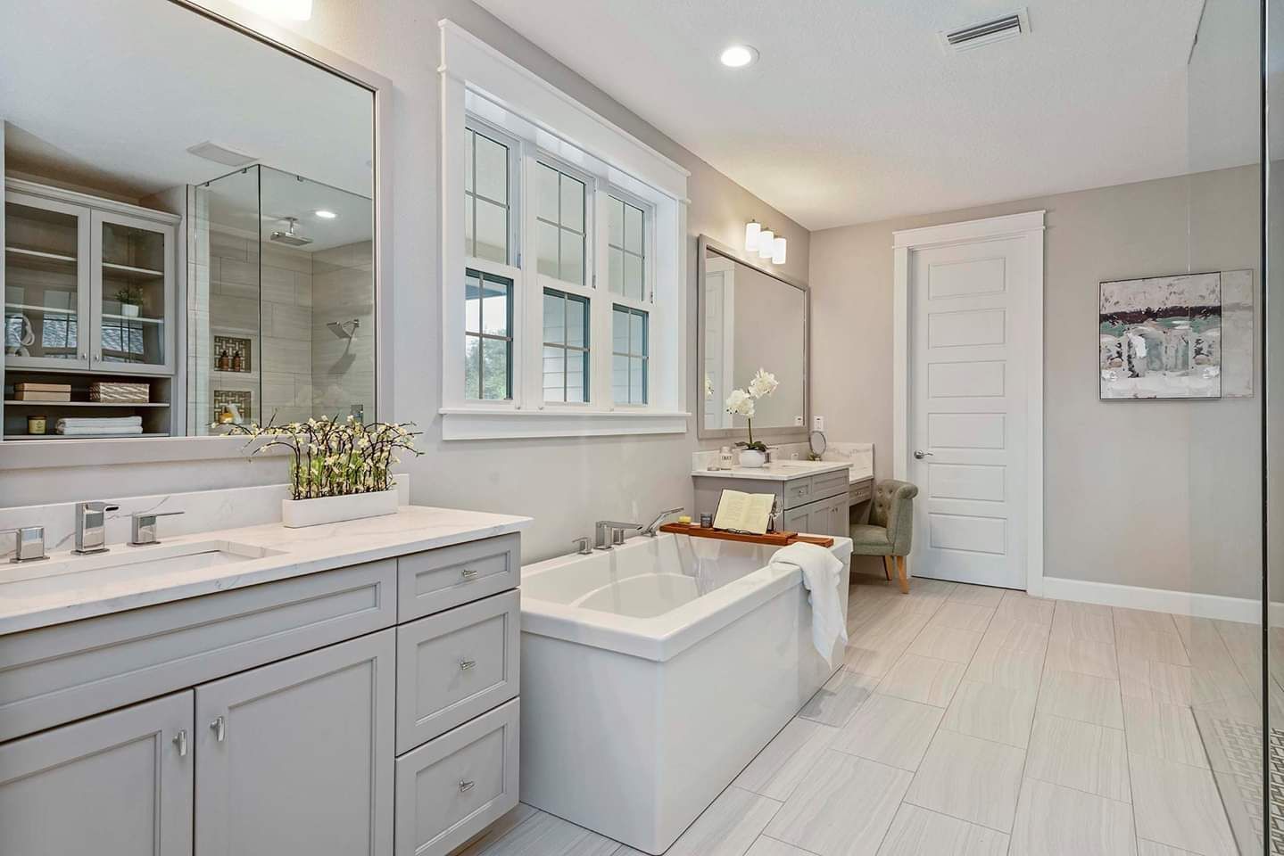 Bright modern bathroom with white vanity, freestanding tub, and large window were present.