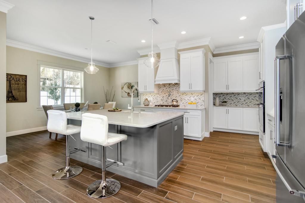 Bright modern kitchen with white cabinets, gray island, stainless steel fridge, and wooden floor.
