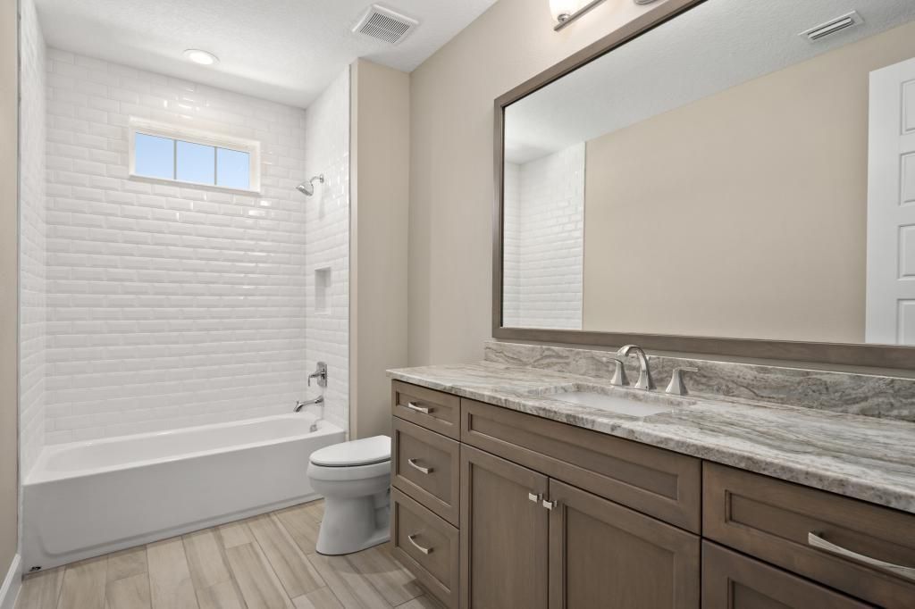 Bright bathroom with a white tub, toilet, and large vanity mirror over a gray countertop.