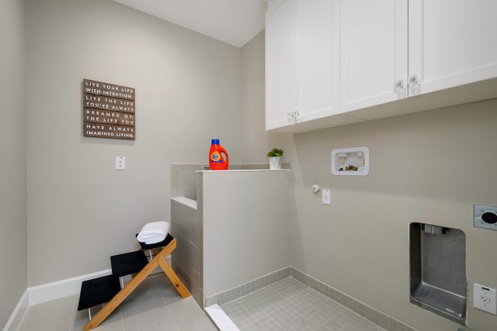 Laundry room with white cabinets, beige walls, and a washer/dryer nook with cleaning supplies.