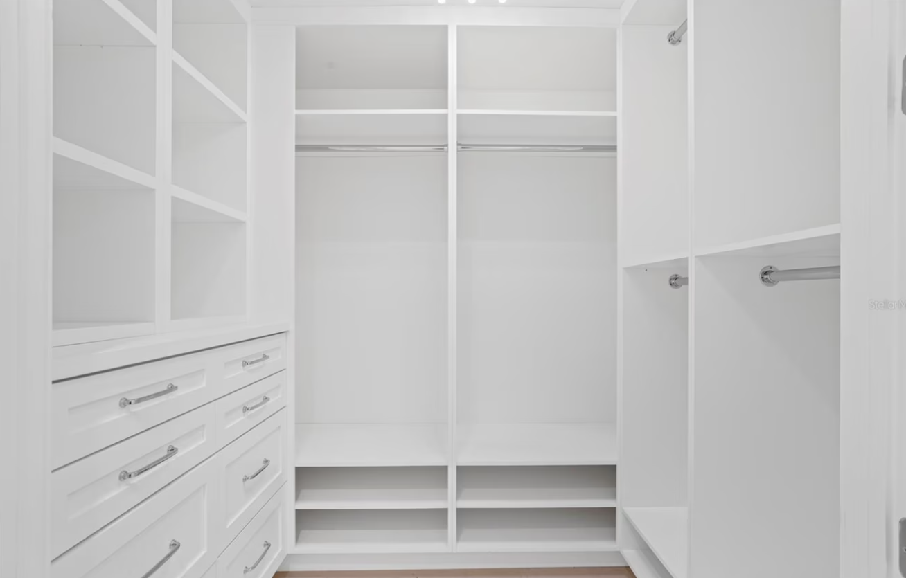 Bright white walk-in closet with shelves, drawers, hanging rods, and shoe cubbies