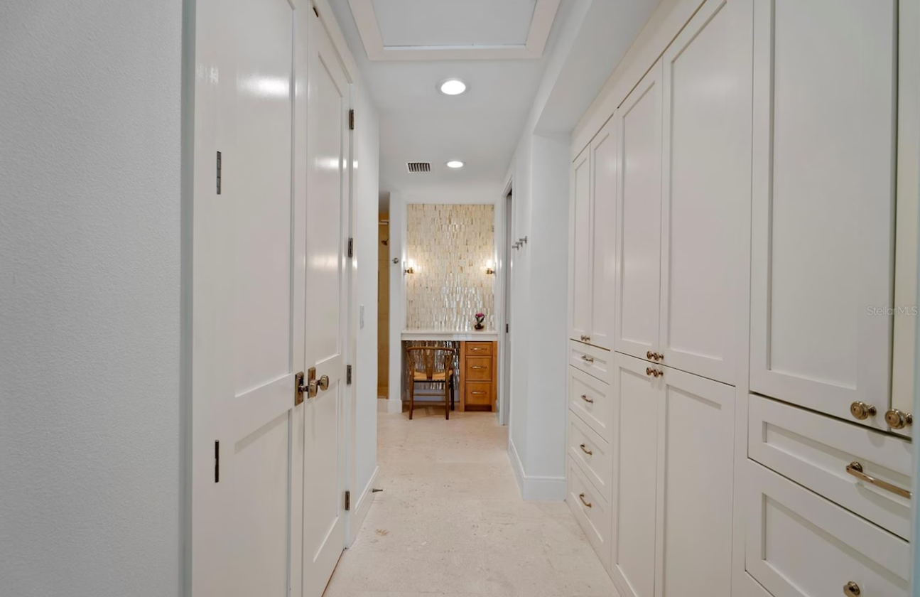 Bright white hallway with built-in cabinets, leading to a dining area at the far end.