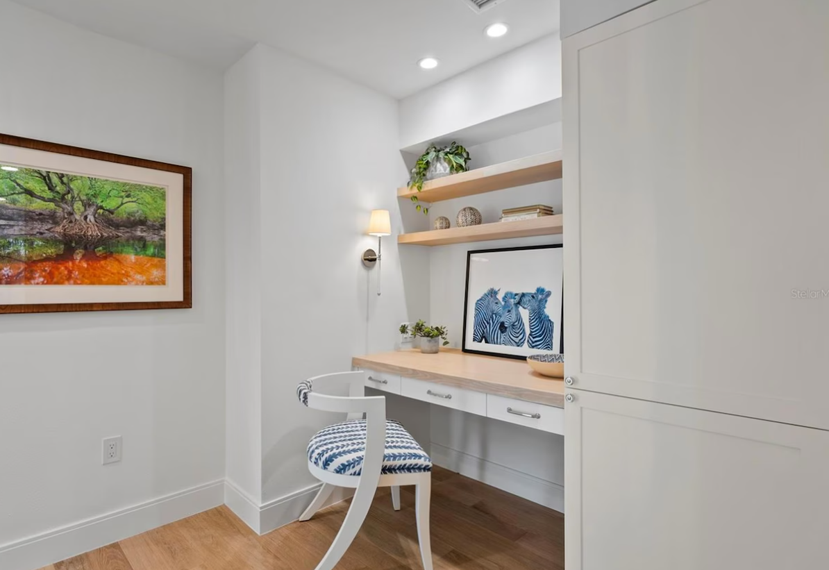 Bright white home office nook with wood desk, floating shelves, chair, and framed blue art