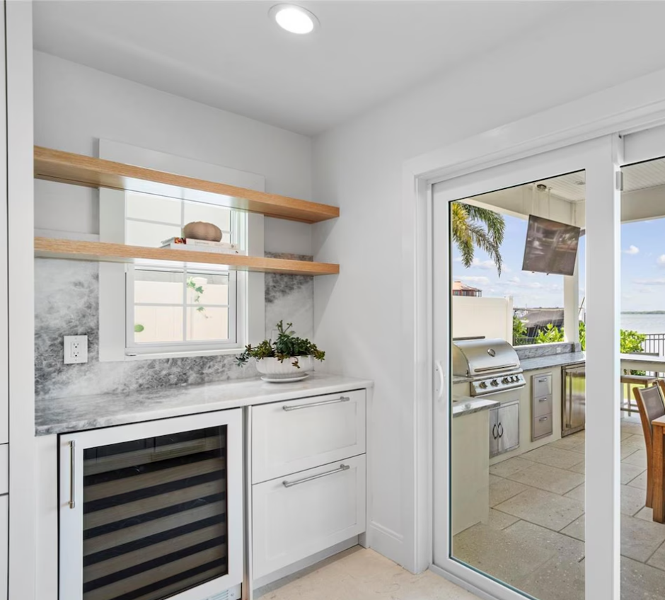 Modern kitchen nook with marble counter, open shelves, wine cooler, and sliding glass door to patio grill area