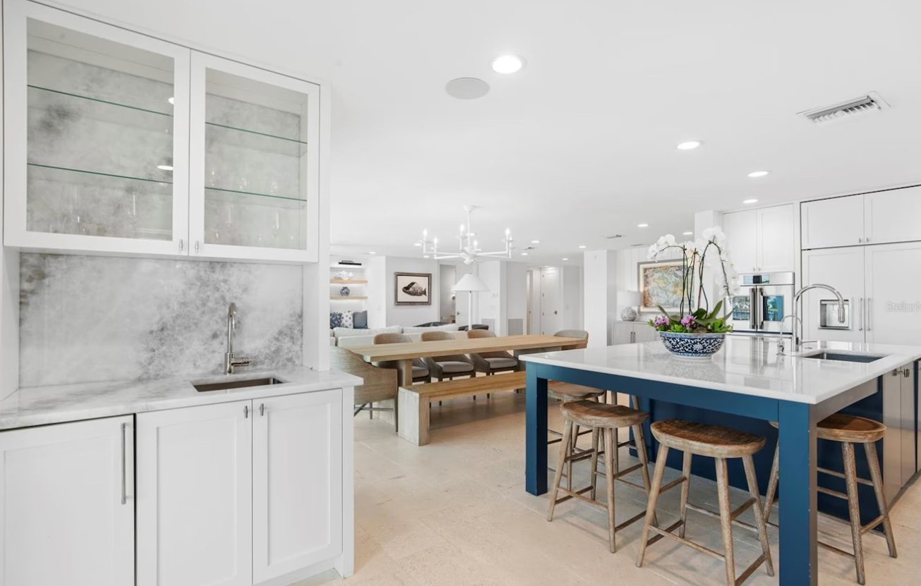 Bright open kitchen and dining area with white cabinets, blue island, and wooden table in a modern home