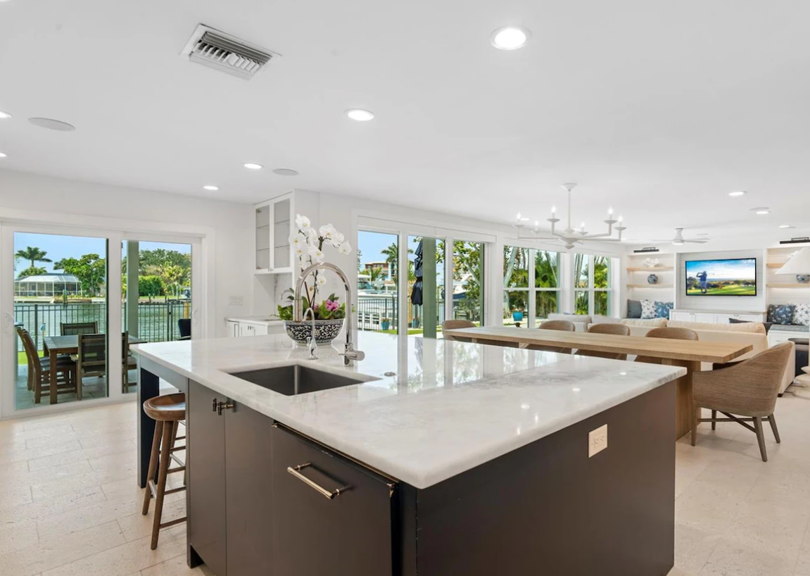 Bright open kitchen and dining area with island, white cabinets, and large windows overlooking greenery
