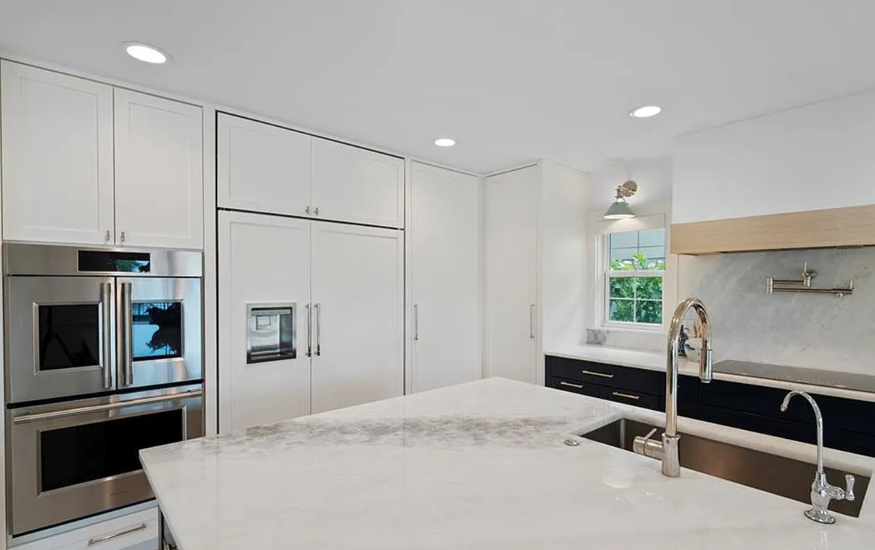 Bright modern white kitchen with stainless appliances, island, and black countertop beneath recessed lights