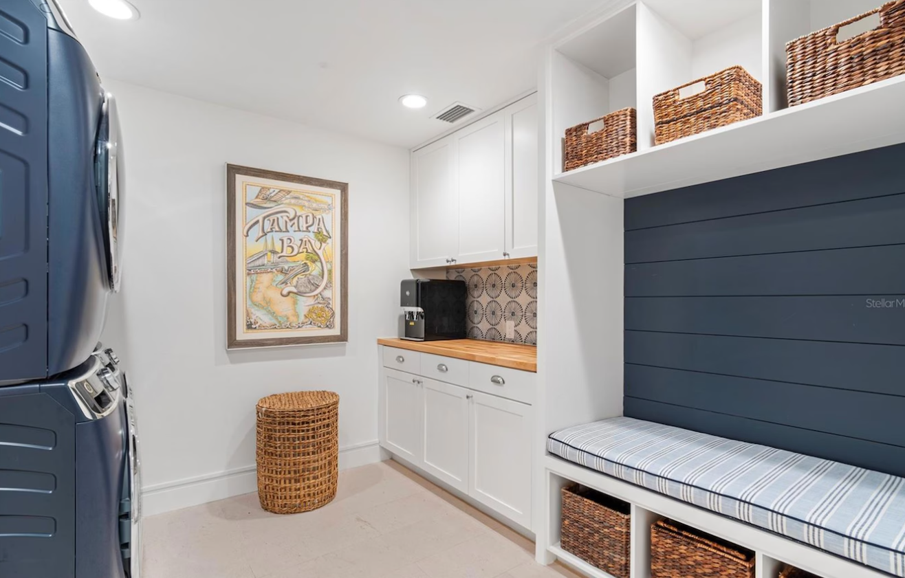 Bright laundry room with blue washer, white cabinets, woven baskets, and built-in bench seating