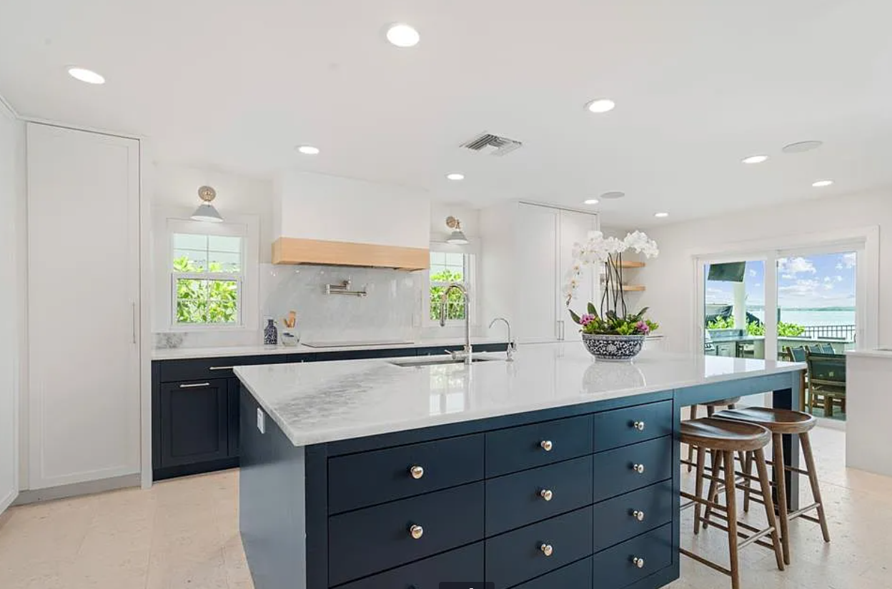 Bright modern kitchen with white cabinets, navy island, and barstools by a window.
