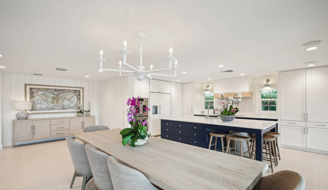 Bright open dining room with long table, blue island, white chairs, chandelier, and floral centerpiece