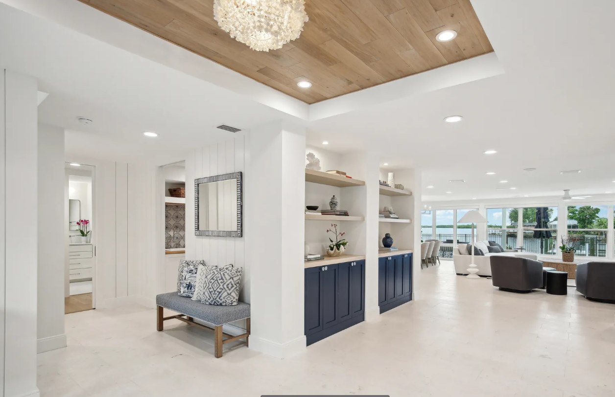 Bright open living room with white walls, wood ceiling, blue bench, and large windows overlooking a patio.