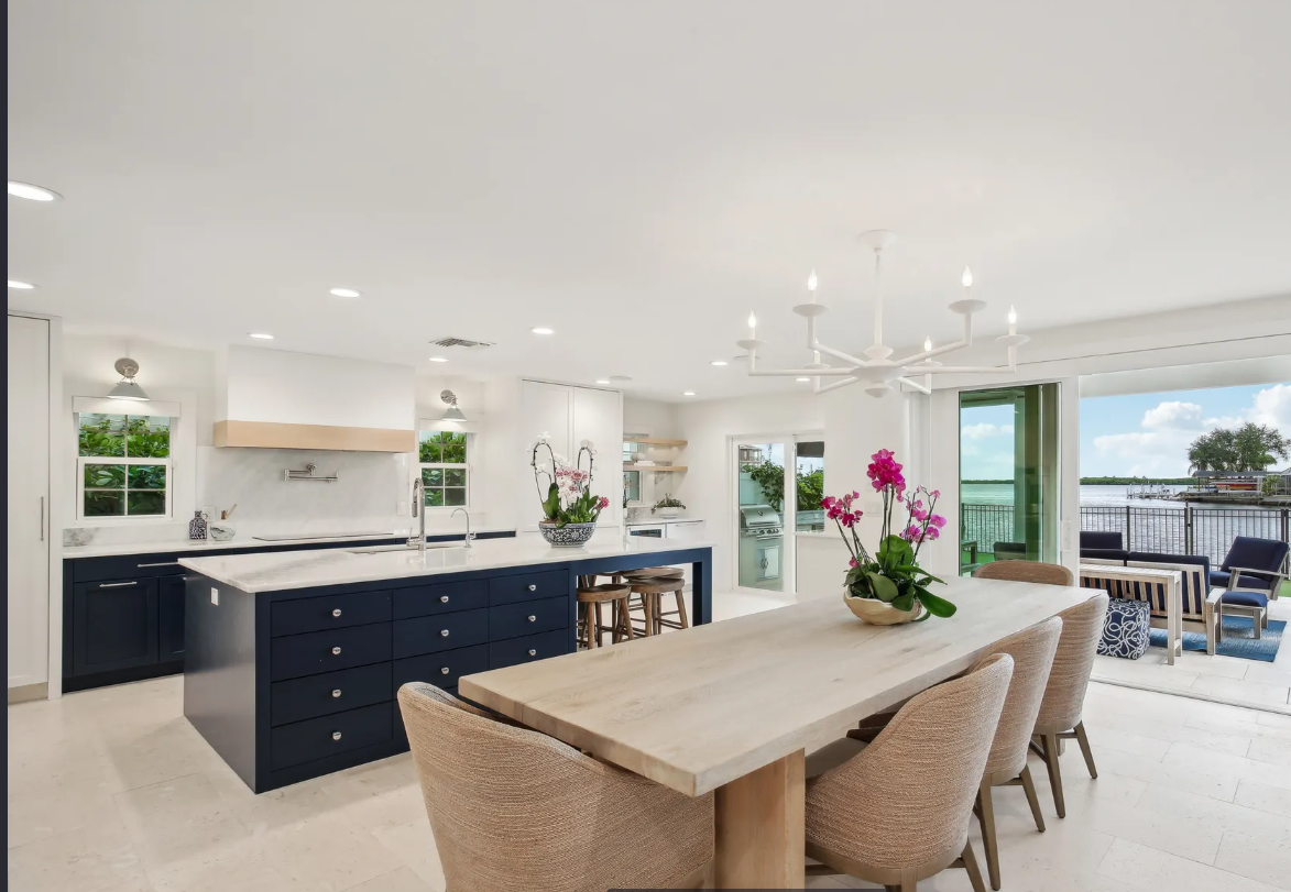 Bright modern kitchen and dining area with white cabinetry, navy island, and large windows to the patio.
