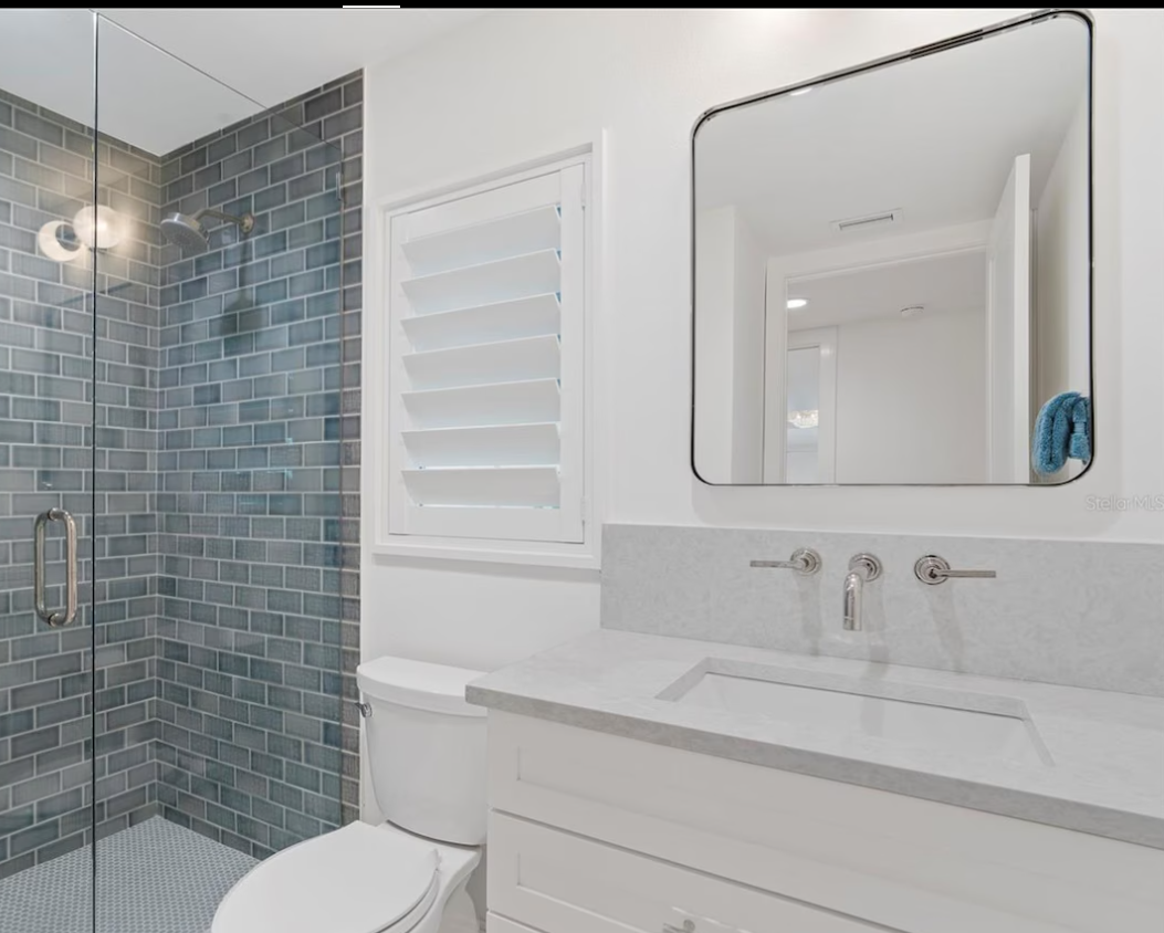 Bright white bathroom with glass shower, blue tile accent wall, vanity sink, and wall mirror