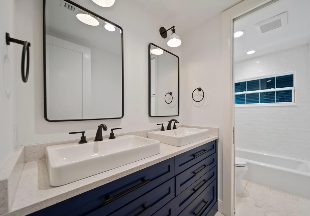 Modern bathroom with double vanity, black fixtures, and a white tub with blue tile accents
