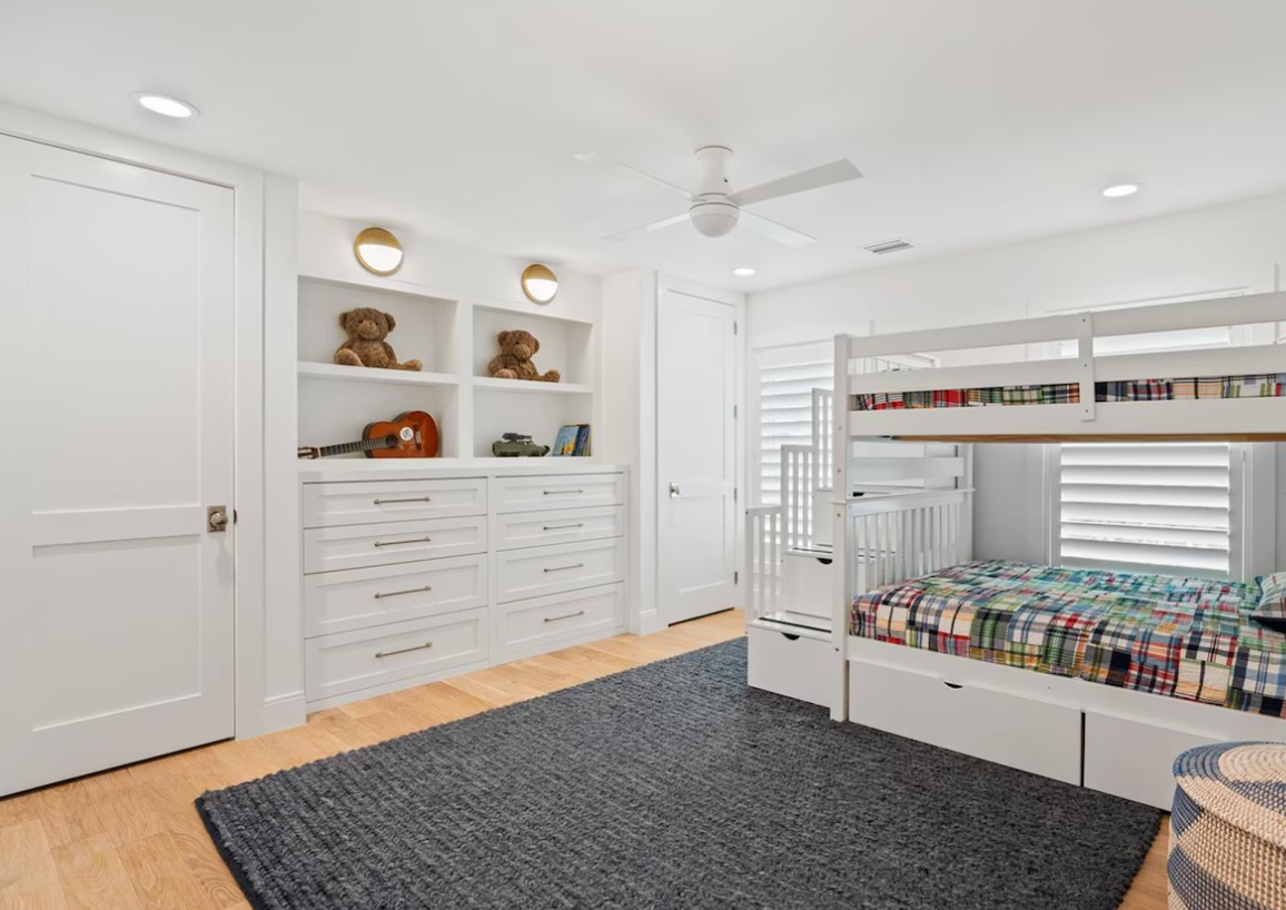 Bright white bedroom with built-in shelves, drawers, twin beds, and a gray rug on wood floors
