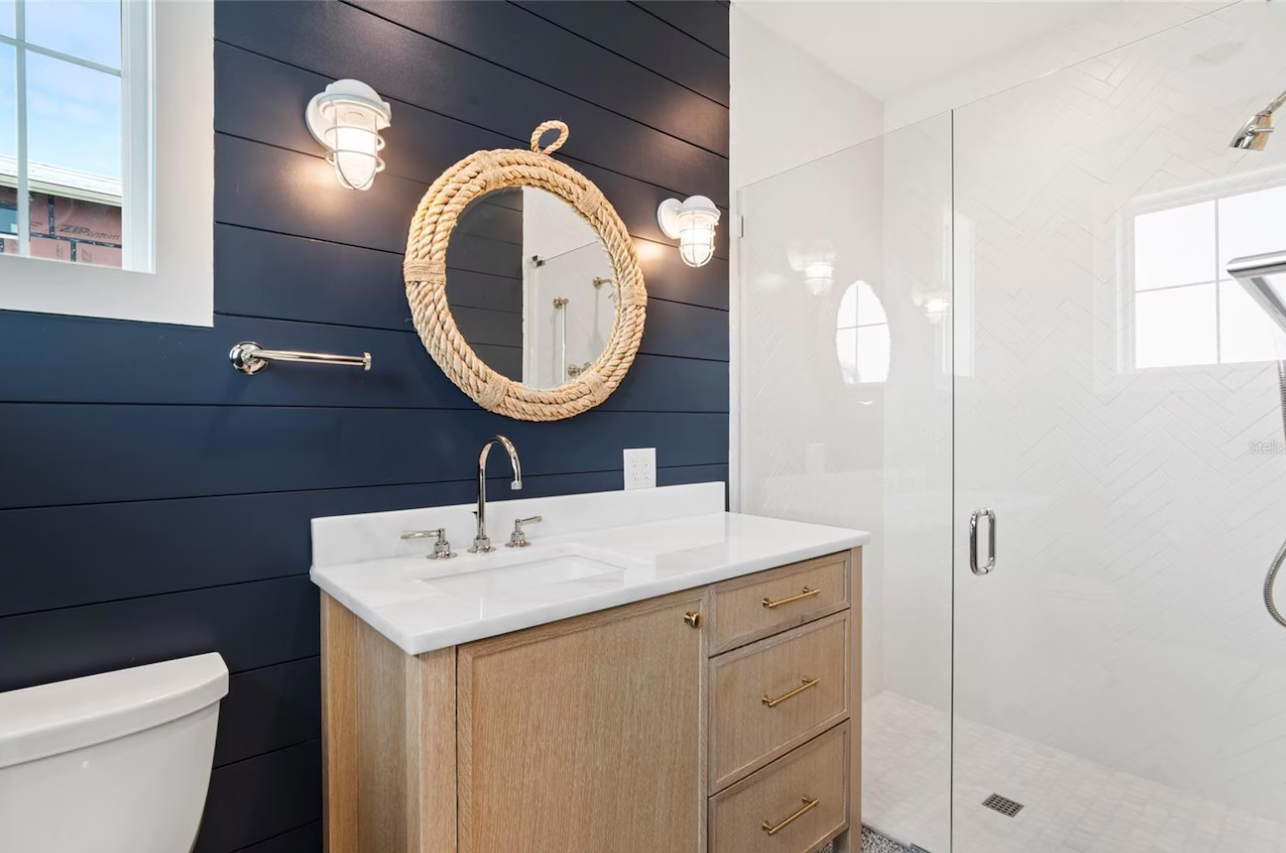 Modern bathroom with navy shiplap wall, round mirror, marble vanity, and glass shower door