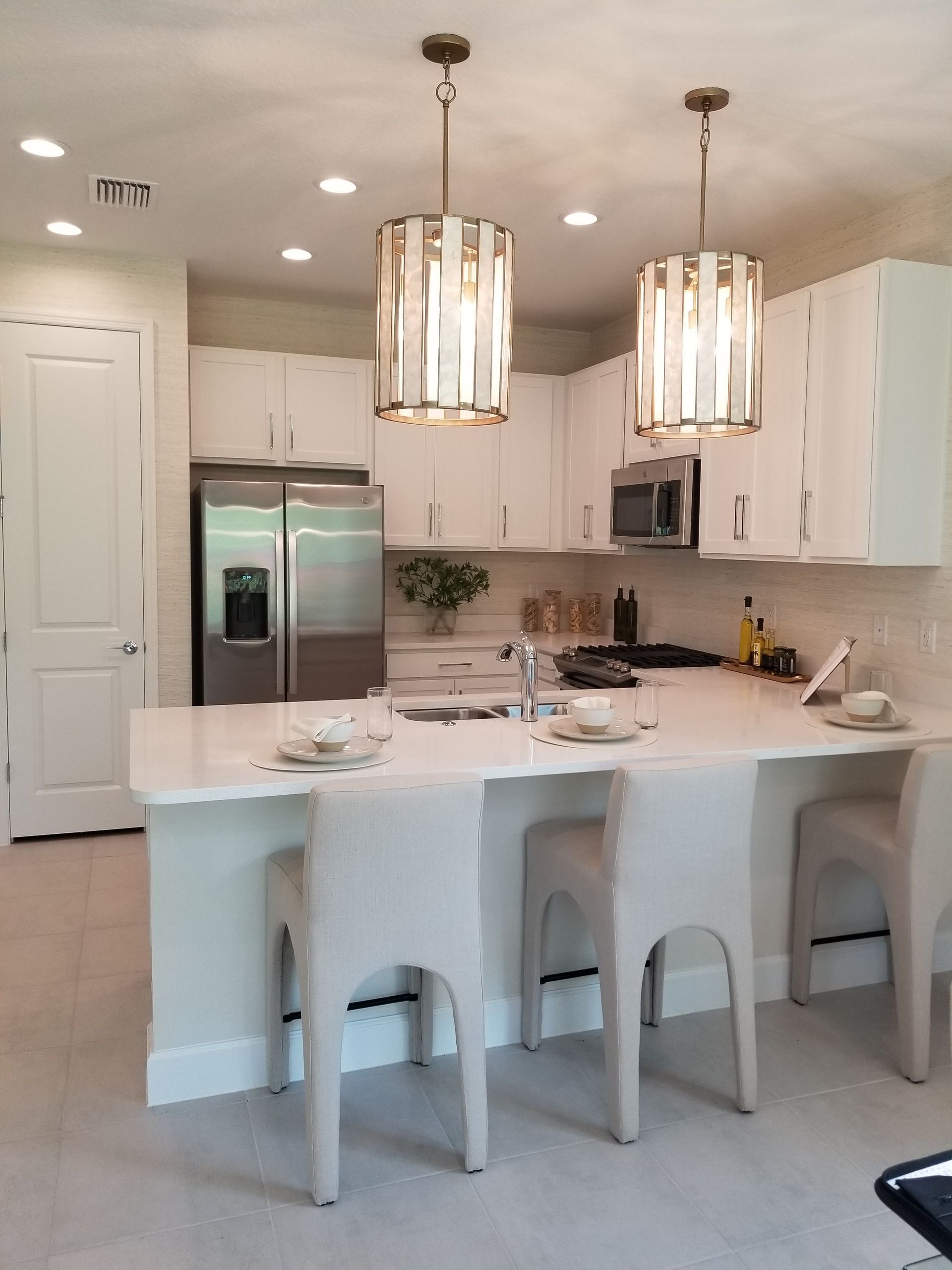 Bright modern kitchen with white cabinets, island, bar stools, and stainless-steel refrigerator