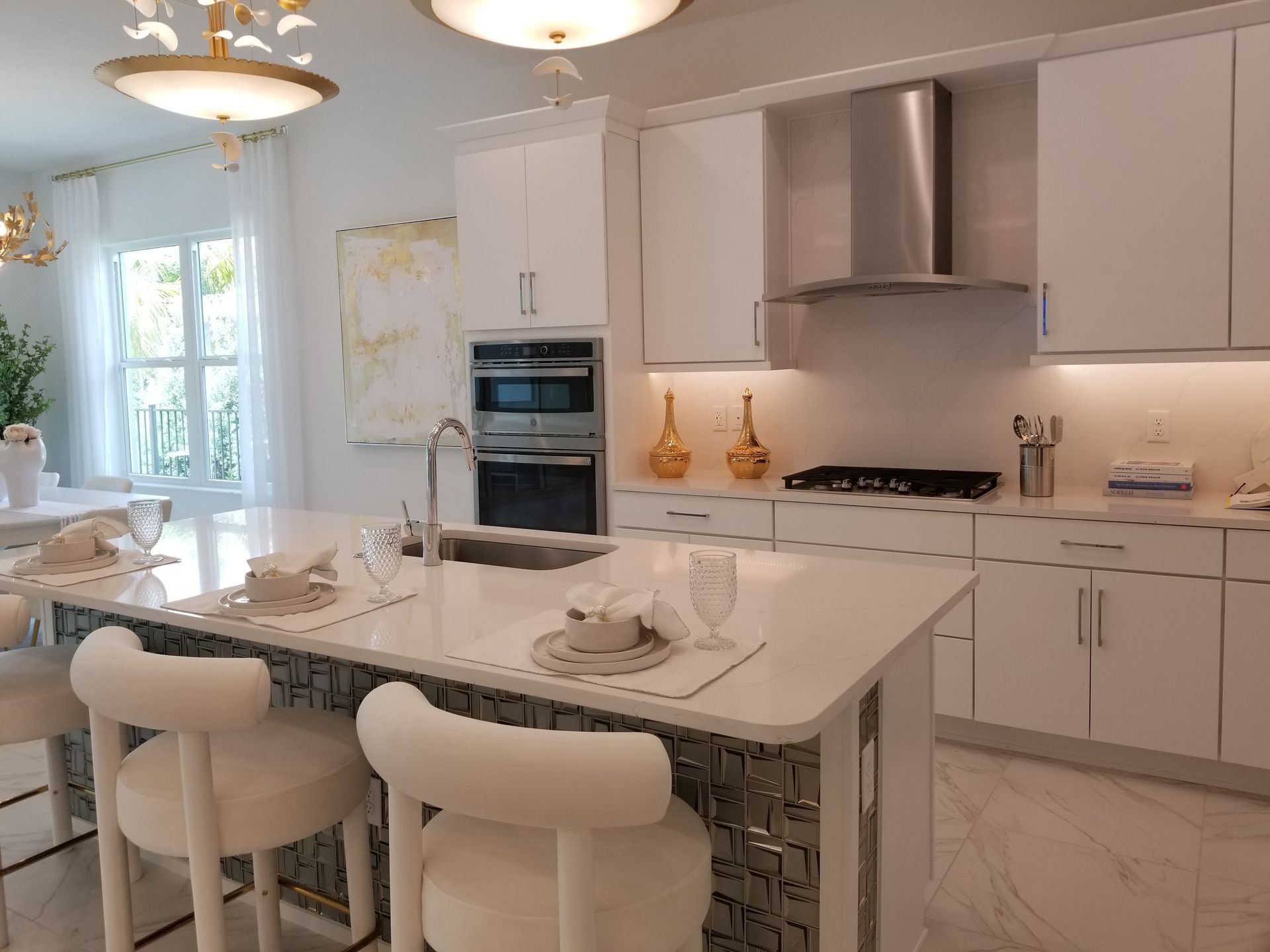 Bright modern white kitchen with marble island, bar stools, pendant lights, and stainless steel appliances