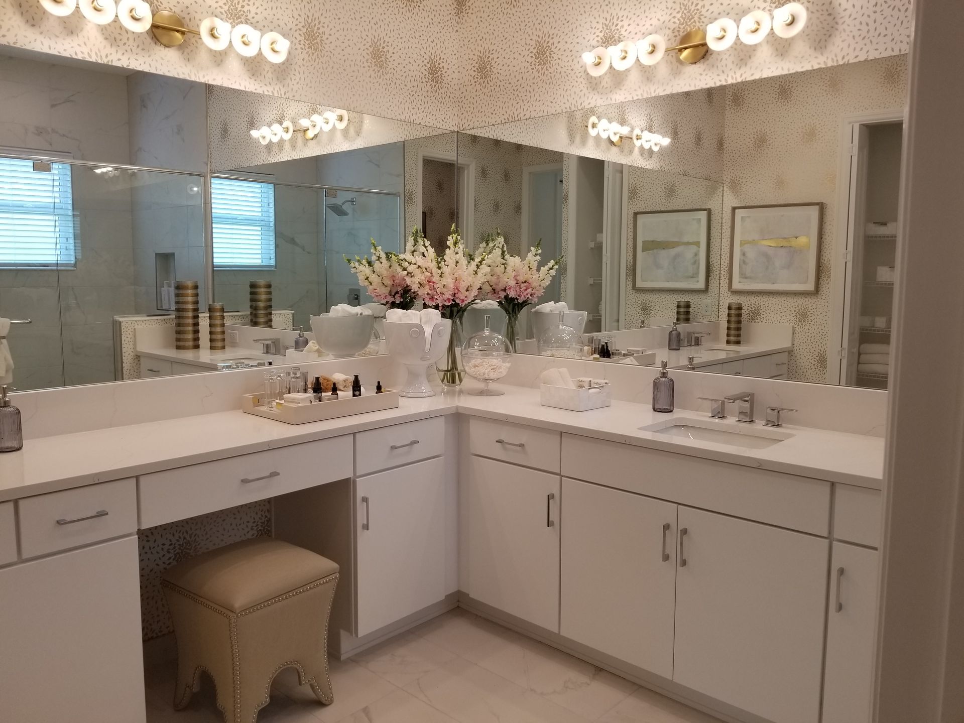 Elegant bathroom vanity with double sinks, mirrors, and pink flowers under bright lights