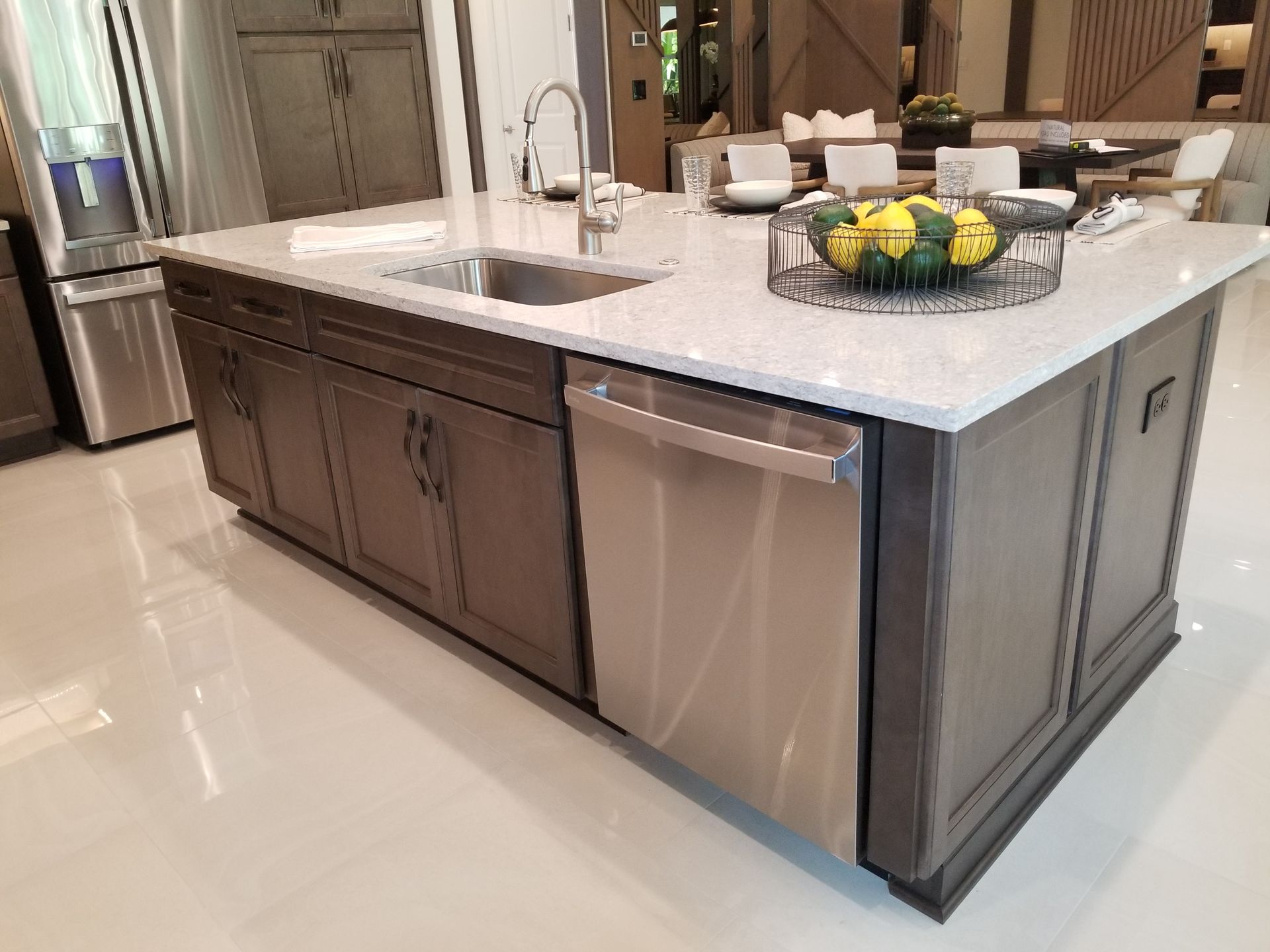 Modern kitchen island with white countertop, dark cabinets, stainless dishwasher, and a fruit bowl
