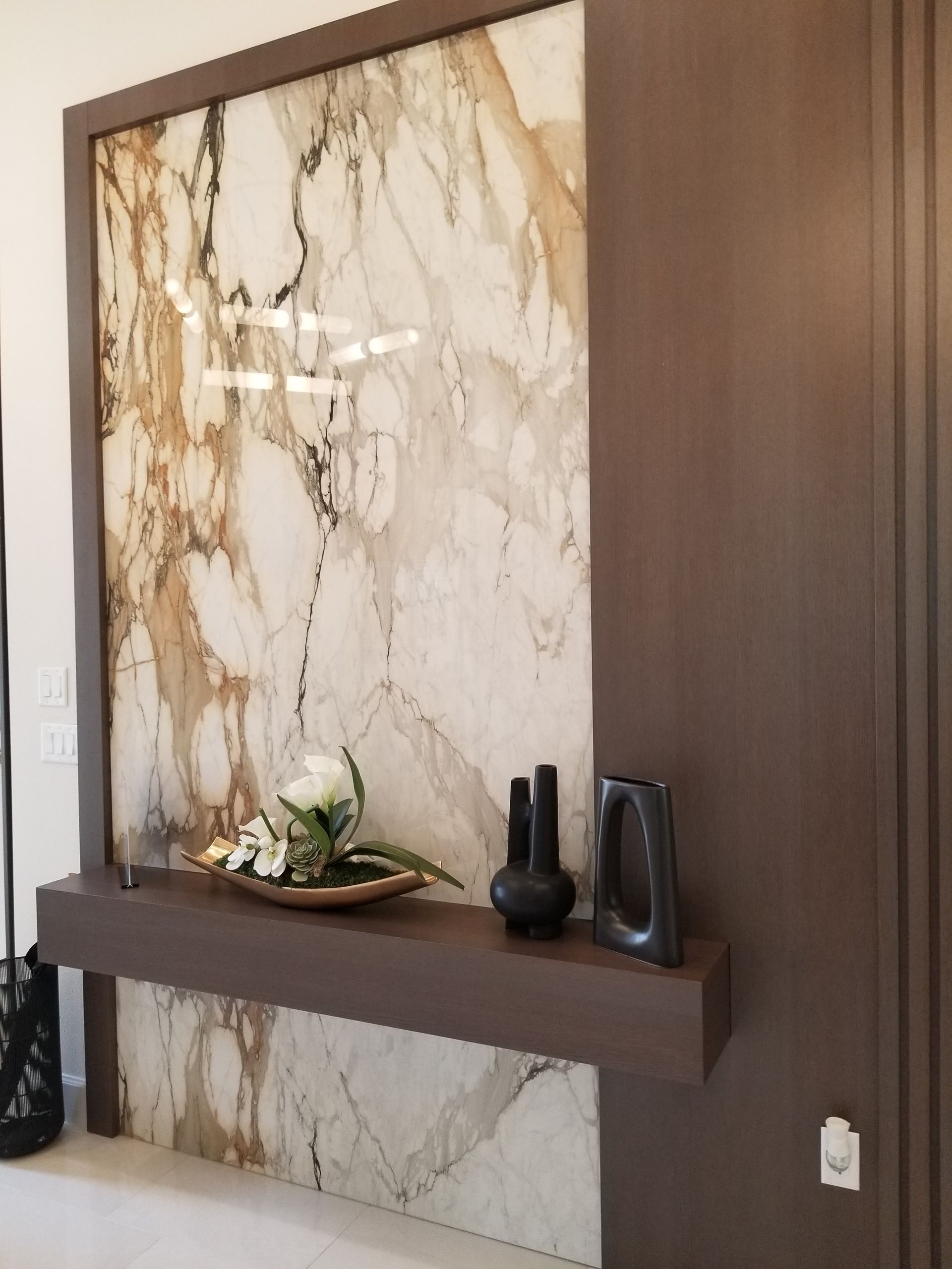 Marble accent wall with a floating shelf holding small decorative vases and a floral arrangement