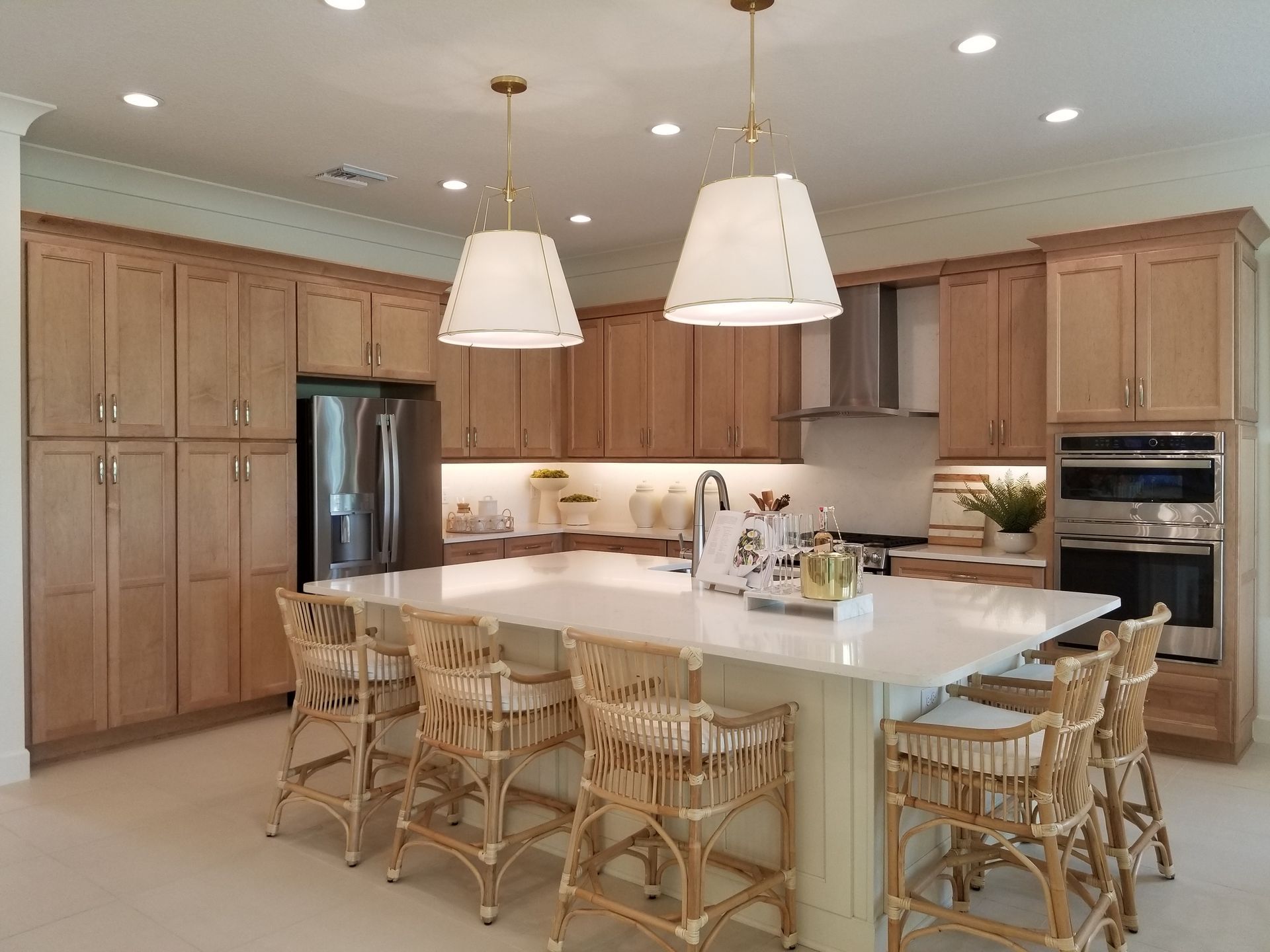 Bright, modern kitchen with a large island, white countertops, wood cabinets, and hanging pendant lights.
