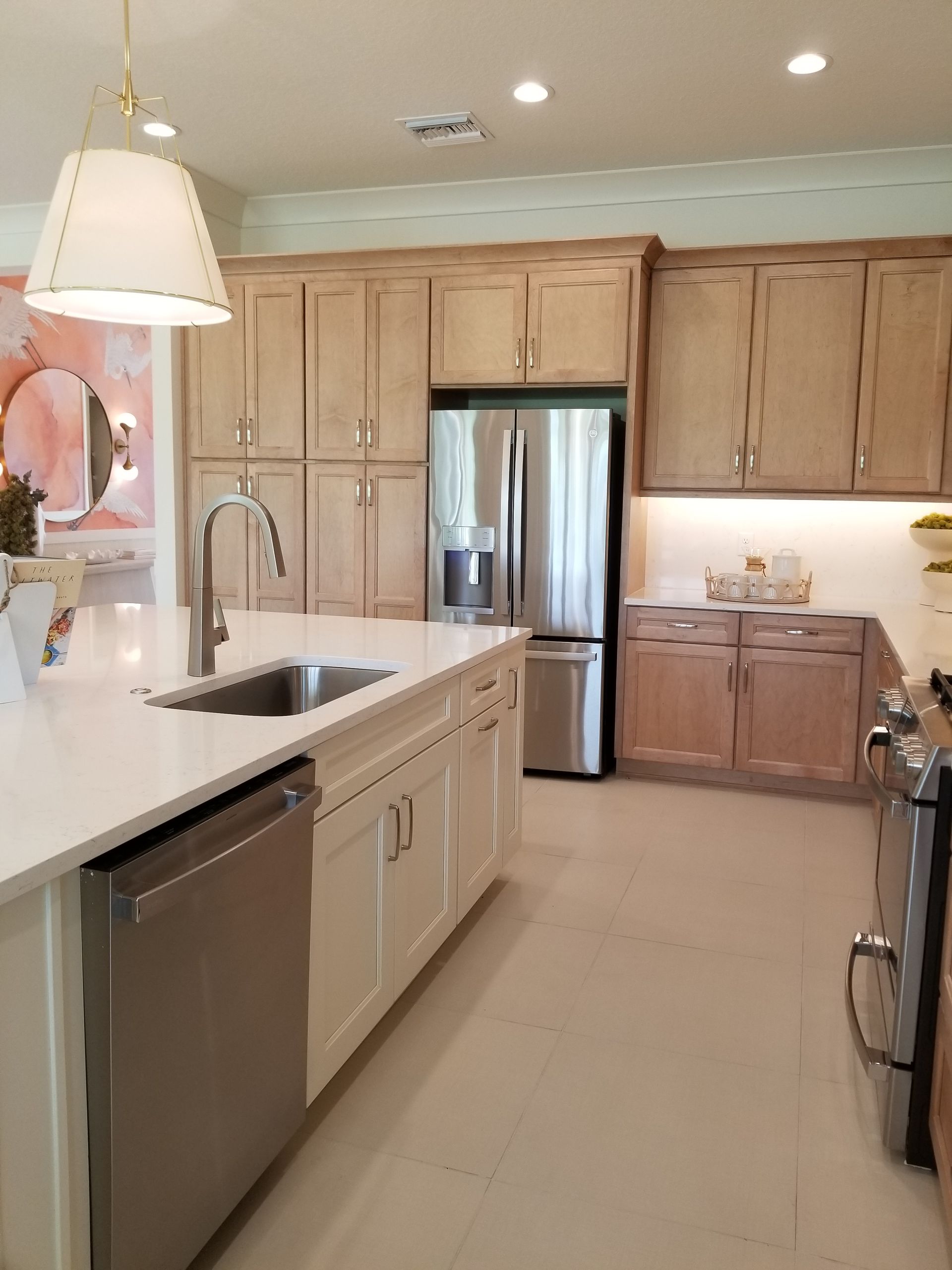 Bright kitchen with light wood cabinets, stainless fridge, white island, and pendant lights.
