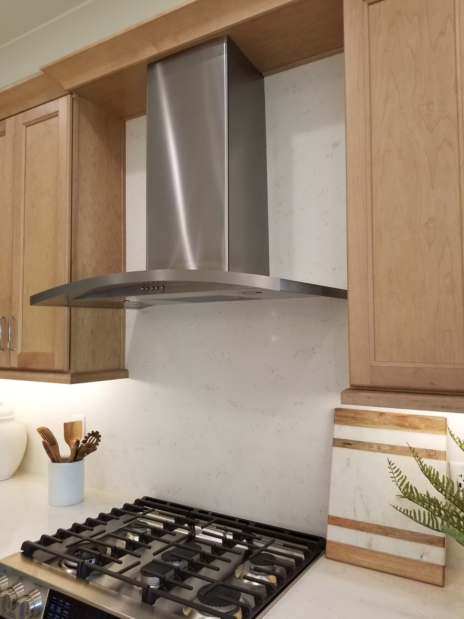Modern kitchen with gas cooktop, stainless range hood, and light wood cabinets