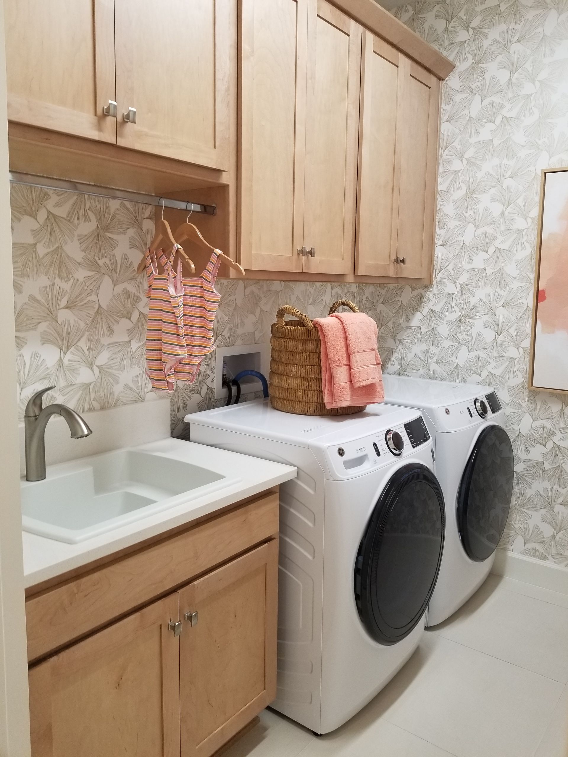 Laundry room with white washer and dryer, wooden cabinets, sink, and woven baskets on top.