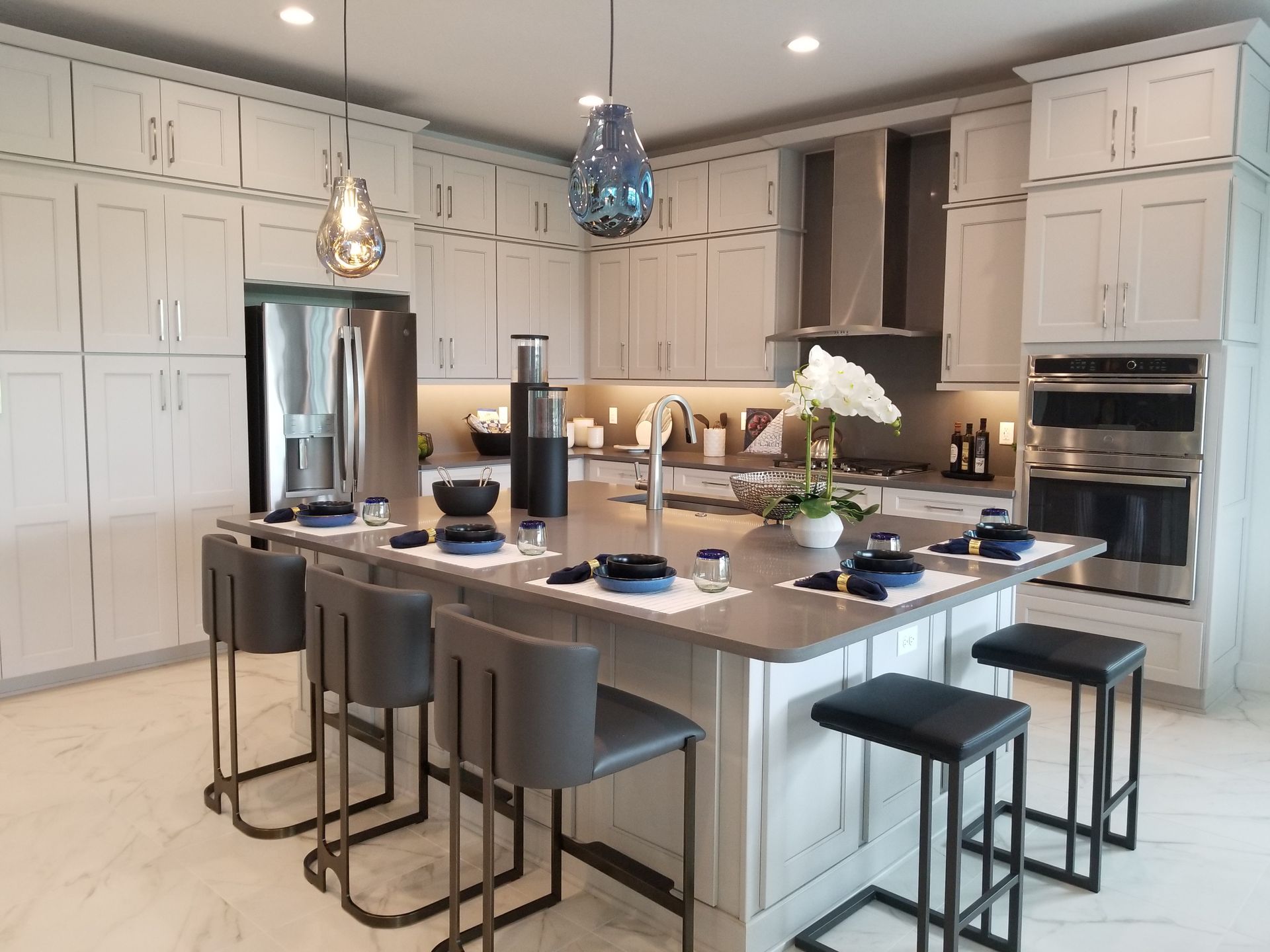 Modern white kitchen with large island, barstools, pendant lights, and stainless steel appliances