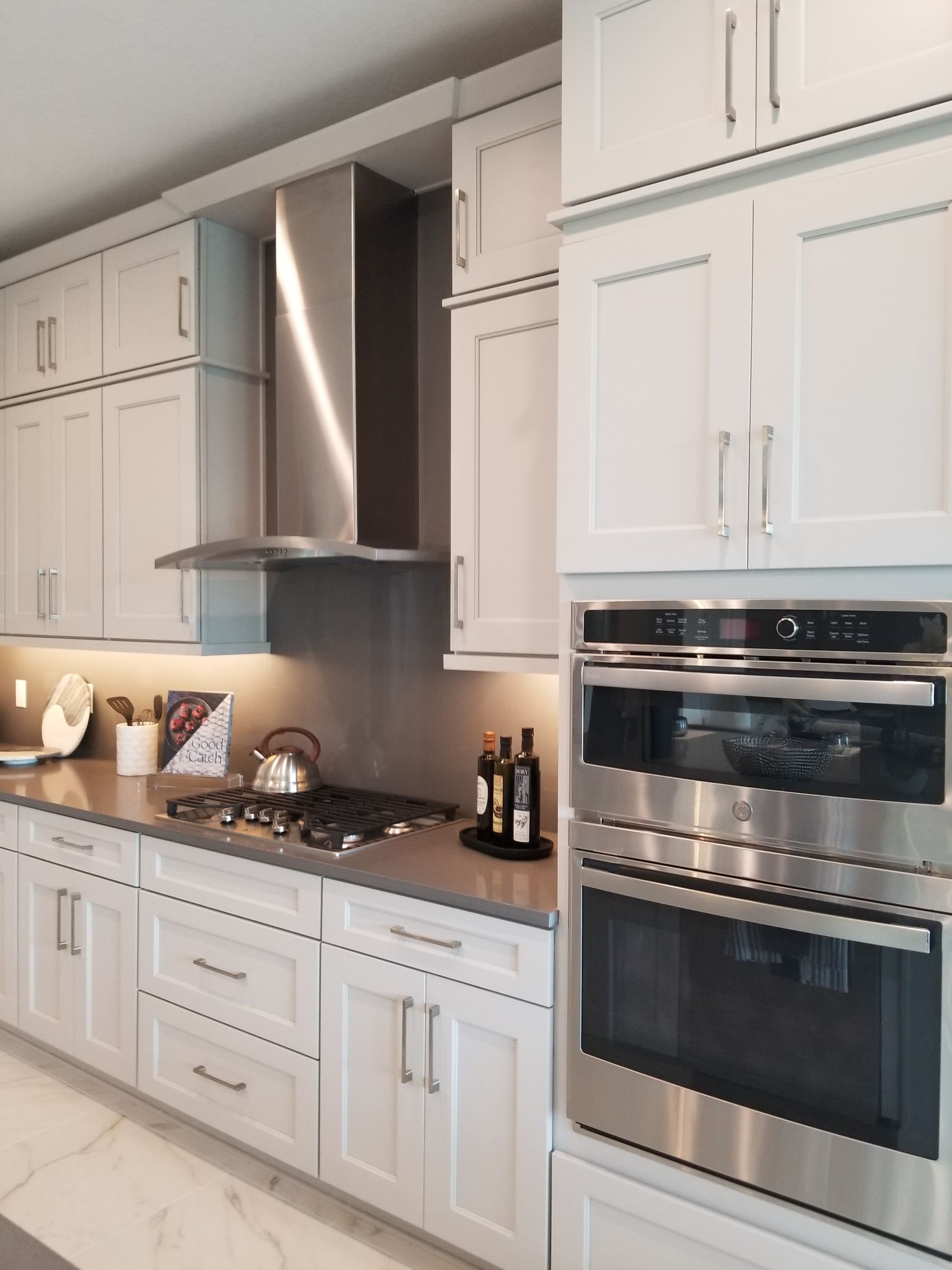 Modern white kitchen with stainless steel range hood, built-in oven, and marble countertops