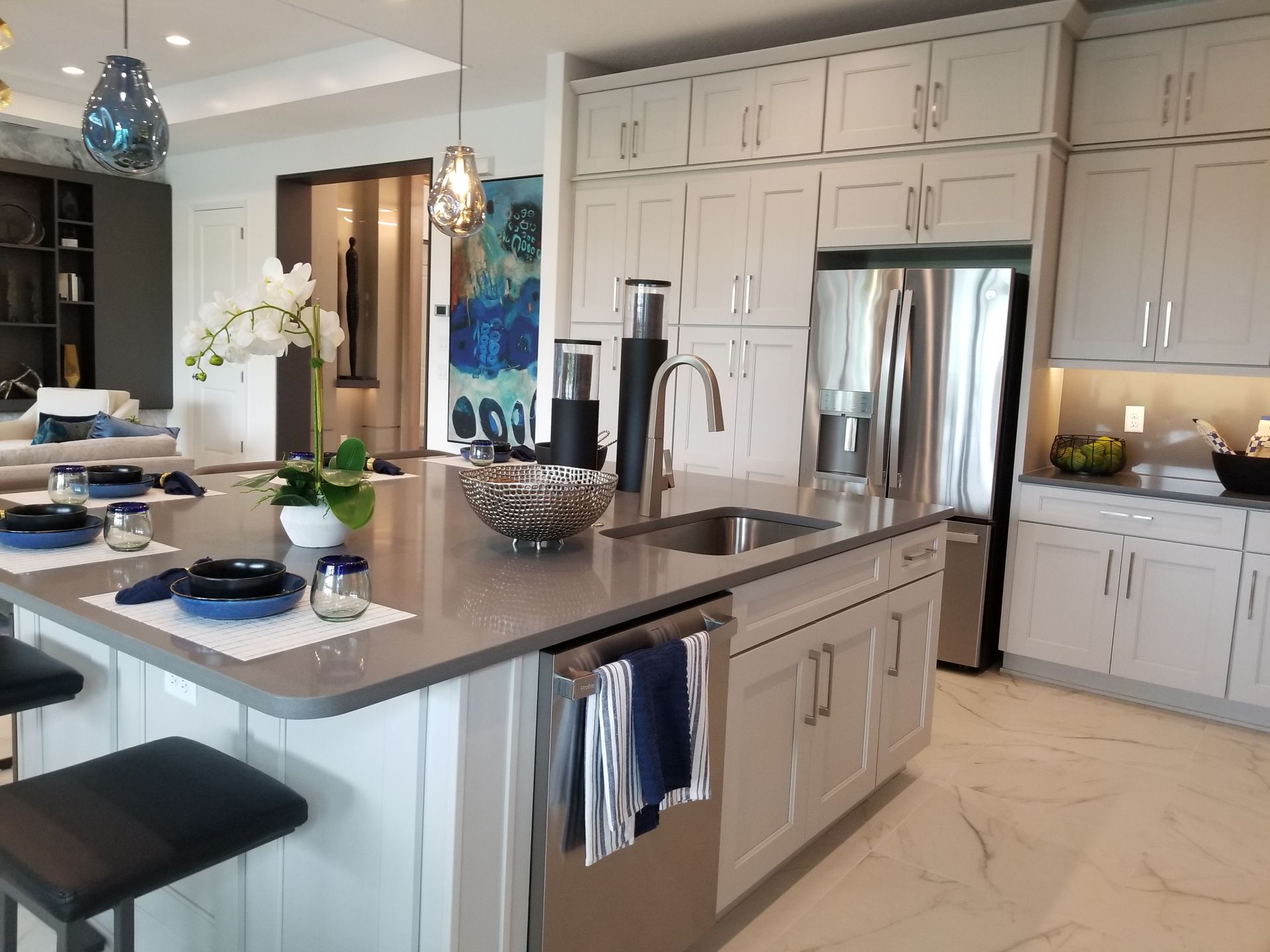 Bright modern kitchen with island, pendant lights, stainless fridge, and white cabinetry