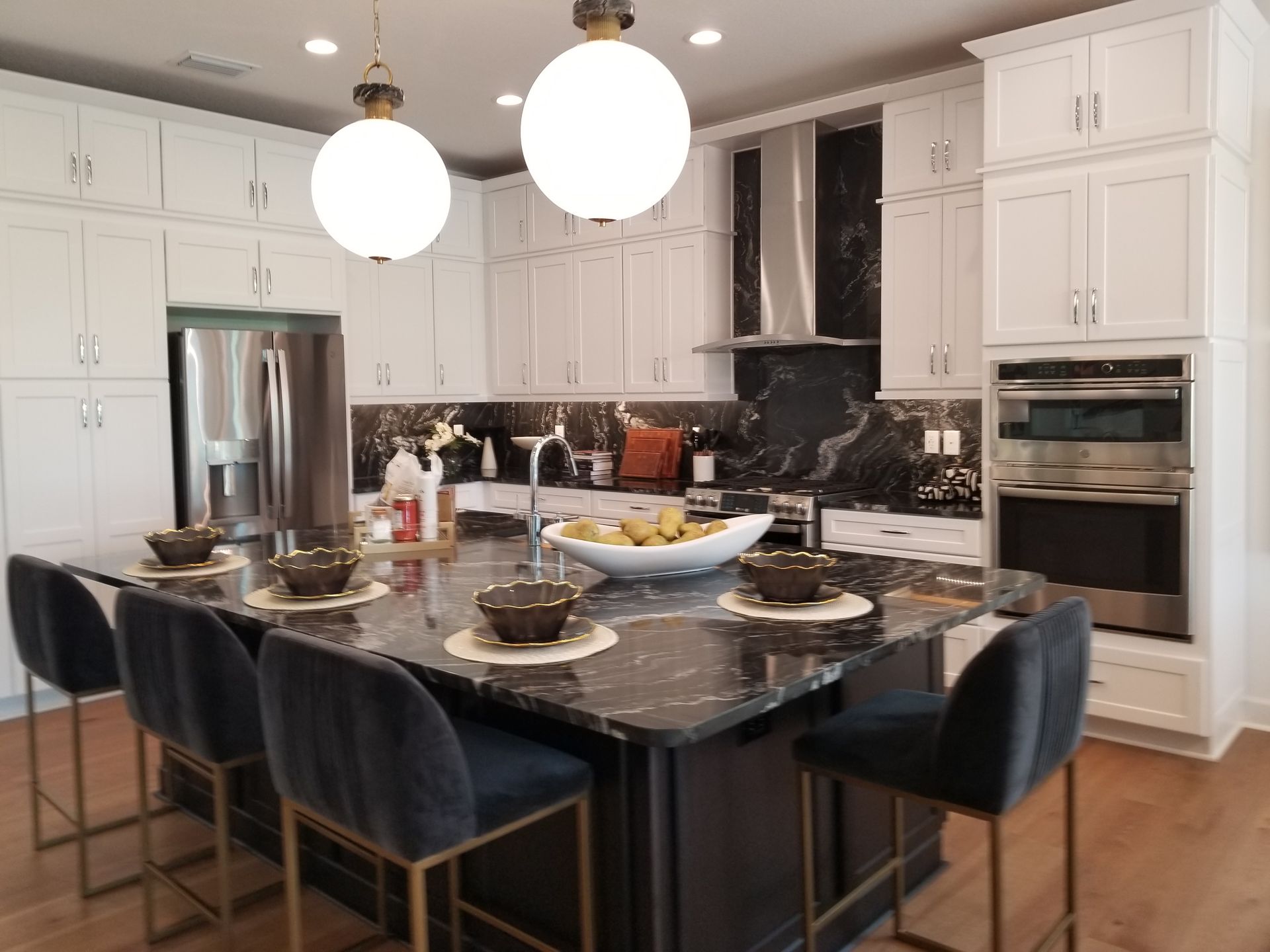 Modern white kitchen with black island, velvet stools, pendant lights, and stainless-steel appliances