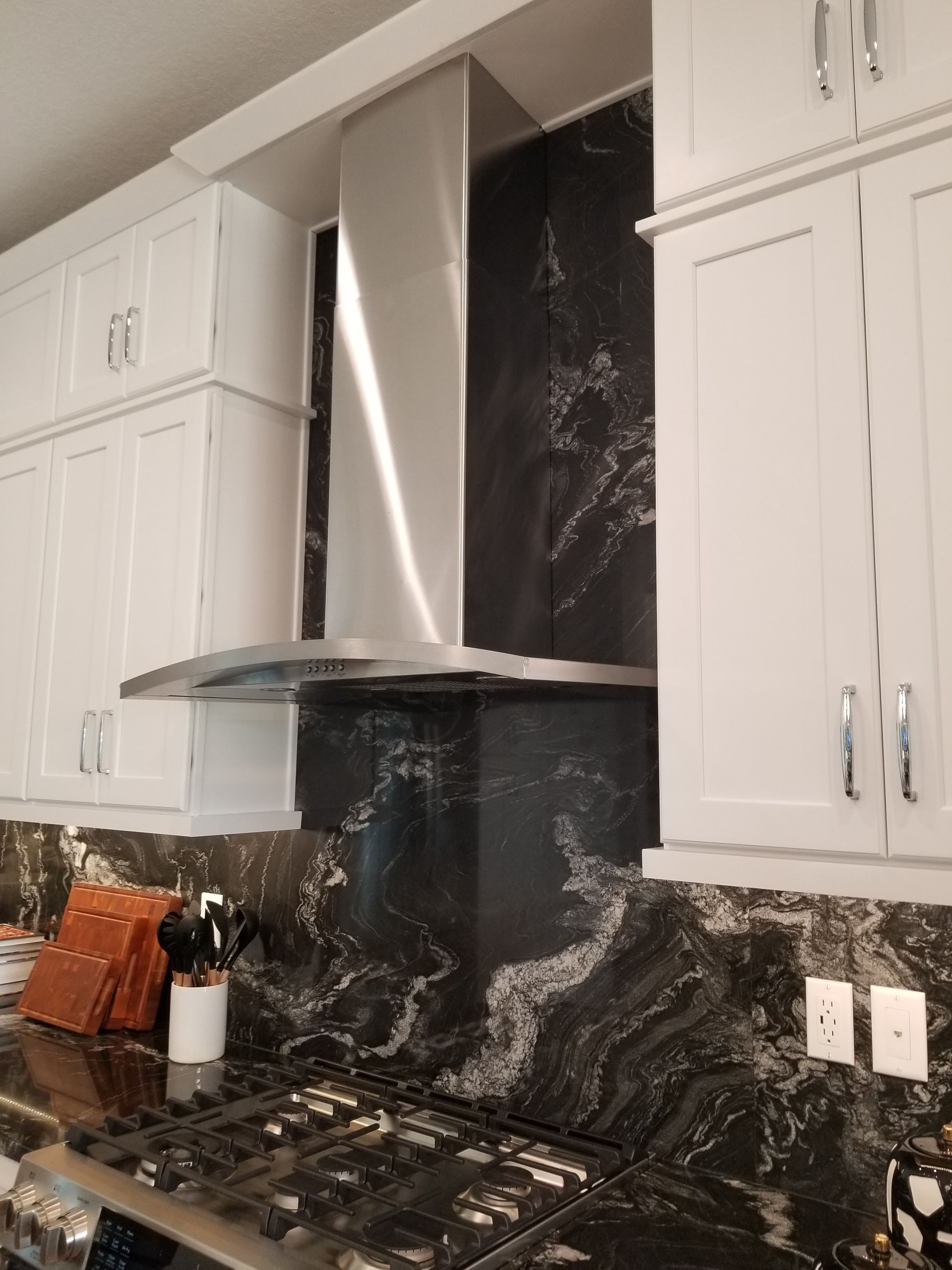 Modern kitchen with white cabinets, stainless range hood, and black marble backsplash around a gas stove.