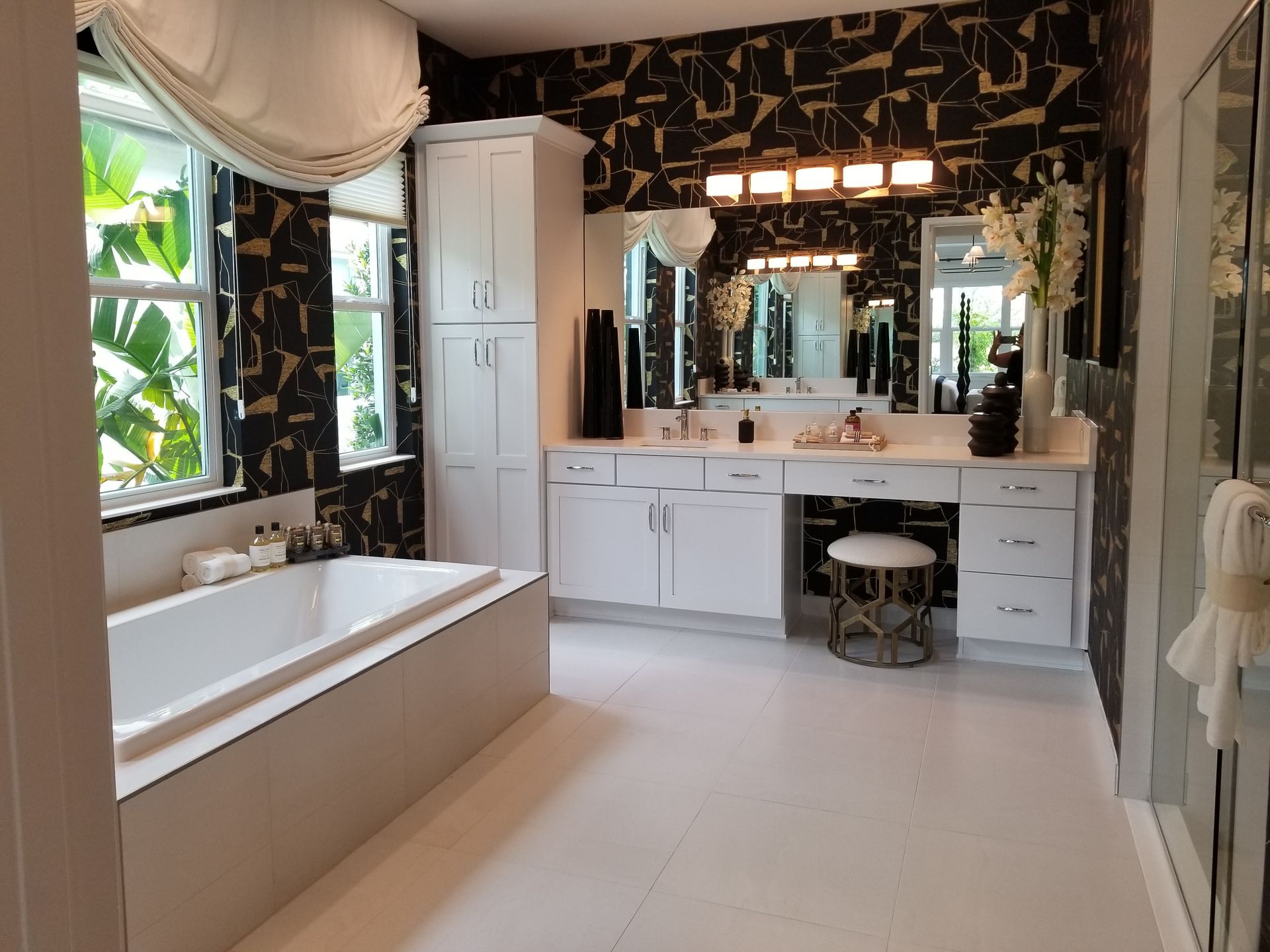 Bright bathroom with a freestanding tub, double vanity, large mirror, and black patterned wallpaper
