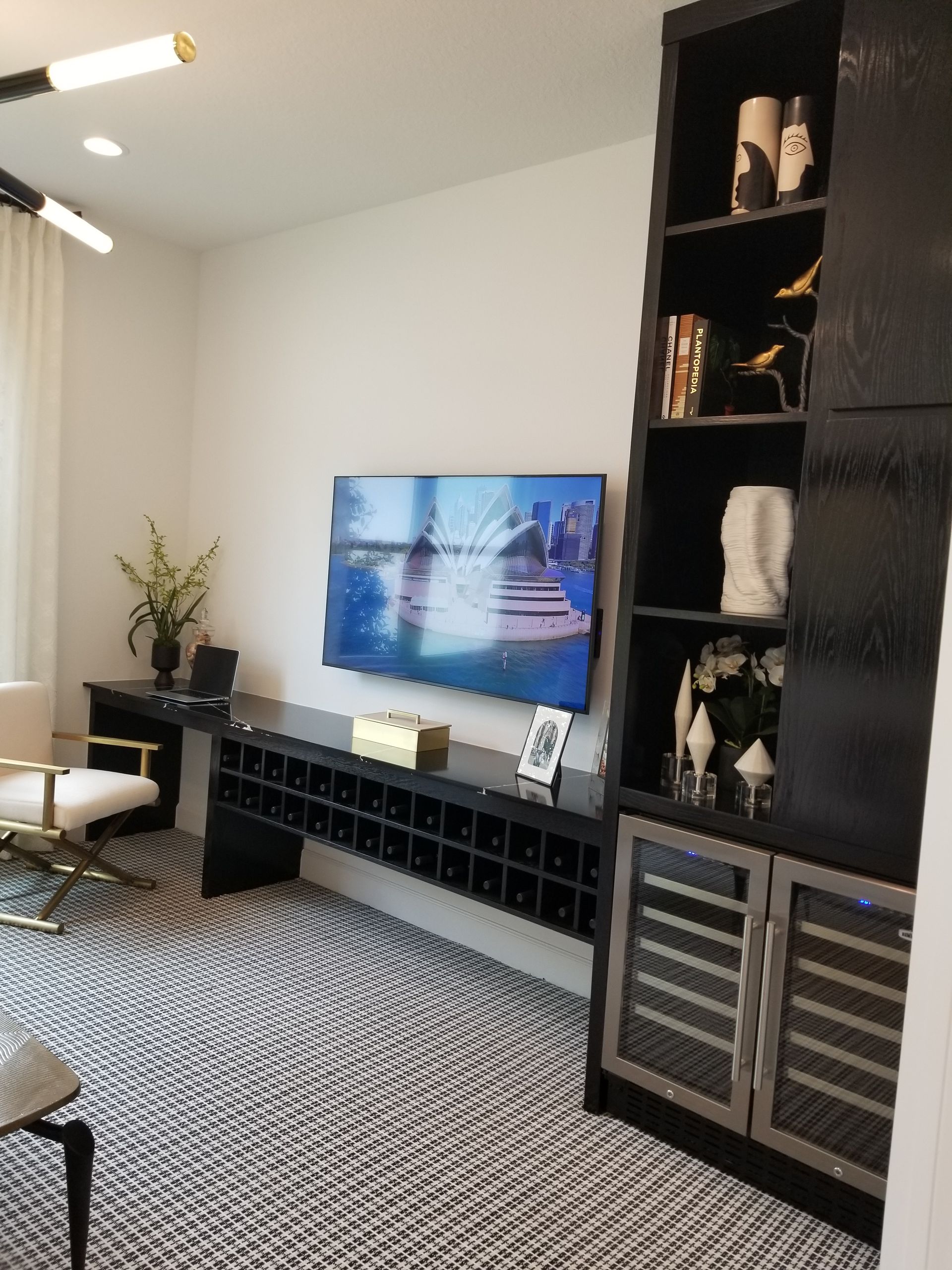 Modern living room with TV on black media console, patterned rug, and tall shelving unit.