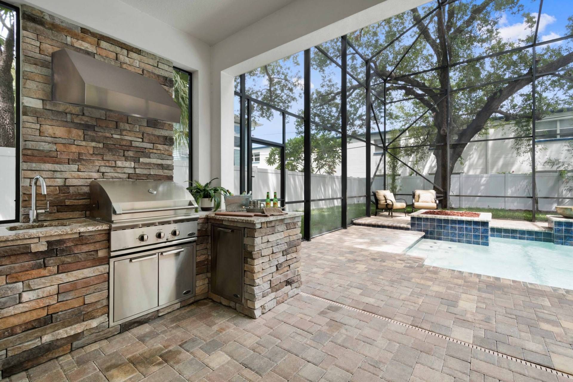 Covered patio with brick outdoor kitchen, pool, and large glass walls overlooking trees