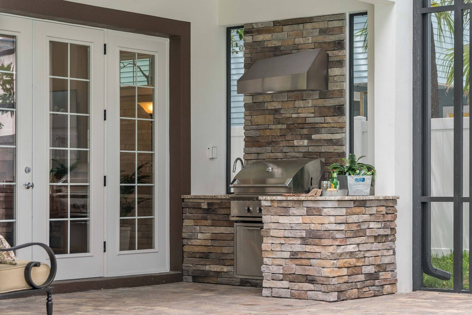 Covered patio with stone outdoor kitchen and French doors leading inside