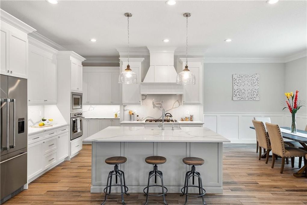 Bright white modern kitchen with island, stools, and adjacent dining area