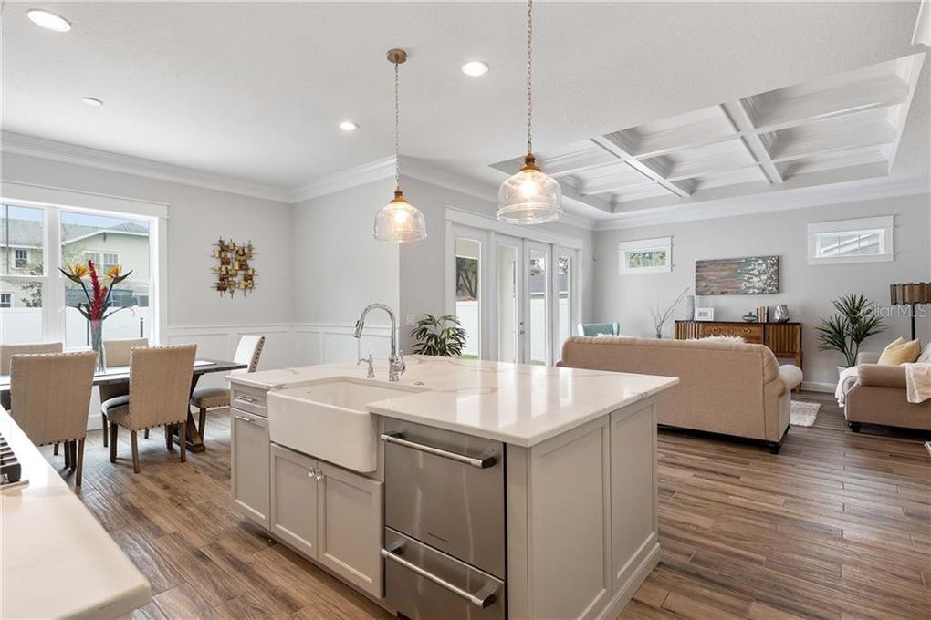 Bright open-plan kitchen and living room with island, pendant lights, wood floors, and beige furniture.